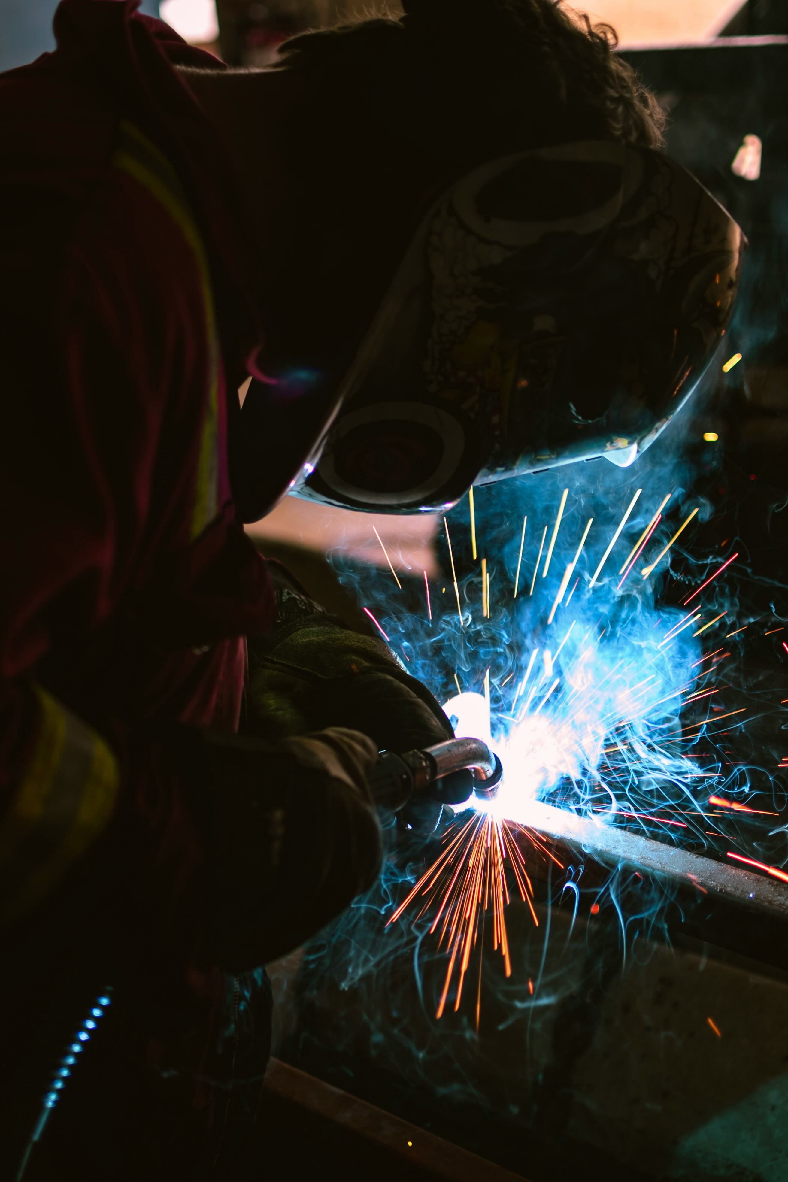 Welder working on a steel project while fumes and smoke arise.