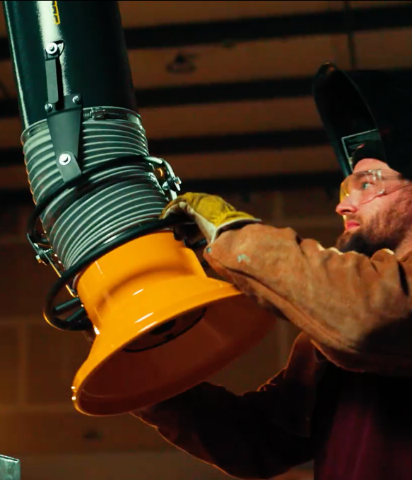 A welder adjusting a Fume Xtractors portable unit to remove welding fumes and smoke from his metalworking project.