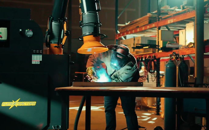 Welder working on a metalworking project while a portable extracts weld fume and smoke.