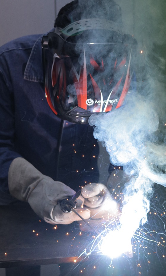 A close up of a welder spot welding while smoke and sparks arise.
