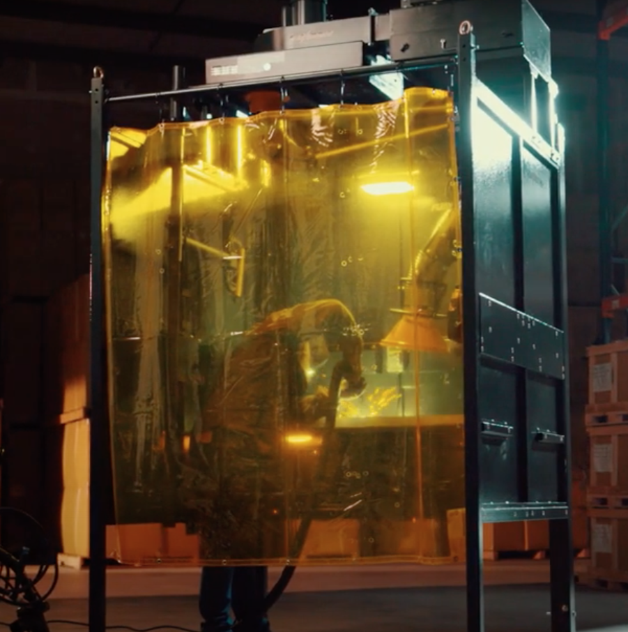 A welder working on a project inside of a Fume Xtractors welding booth while a fume arm works to remove fumes.