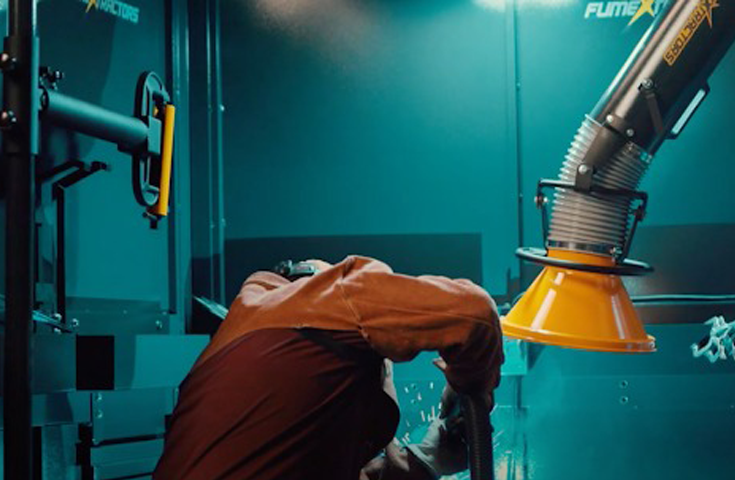 Machine operator working inside of a welding booth while a fume arm extracts fume and smoke.