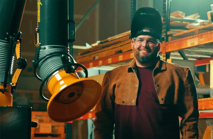 A machine operator in PPE gear standing next to a fume extraction arm that can be used for welding and grinding applications.