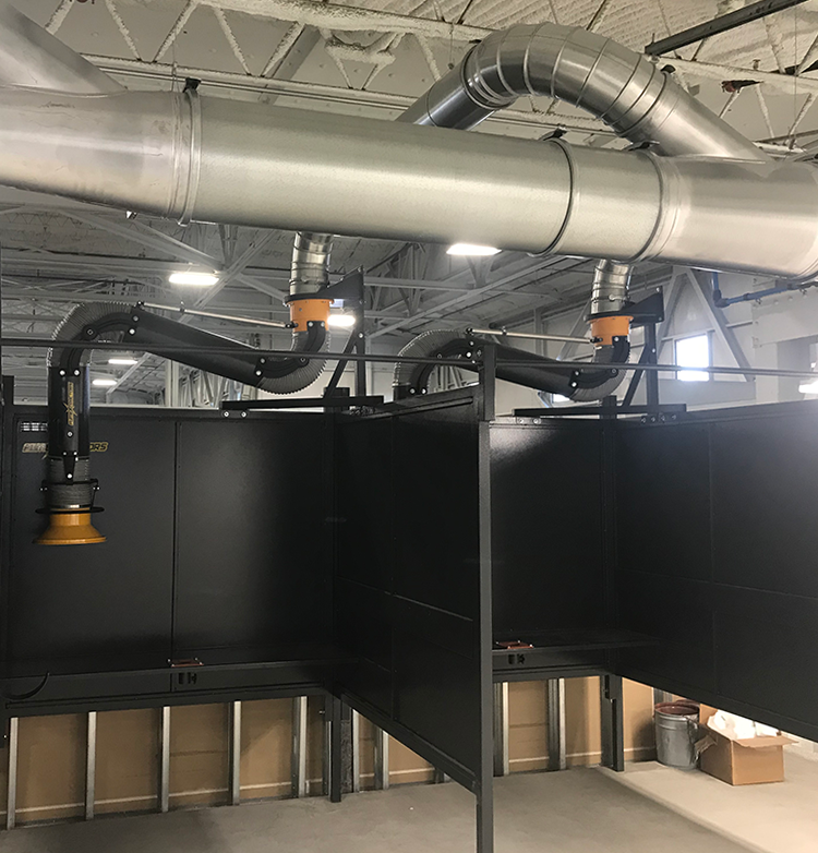 Welding booths side by side in an industrial facility, both equipped with fume extraction arms.