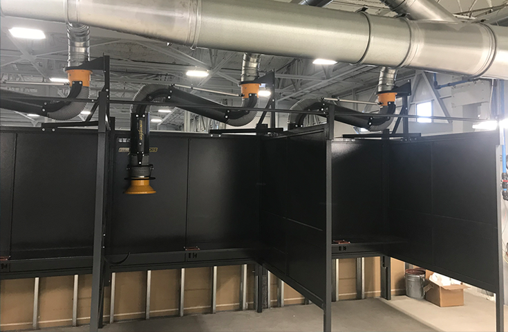 A series of three welding booths equipped with hanging fume extractor arms shown installed in an industrial facility.