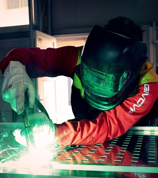 A machine operator welding on aluminum while smoke and fumes arise.