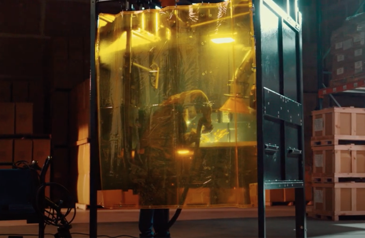 Machine operator working on a project inside of a Fume Xtractors welding booth while a fume arm extracts smoke and fumes.