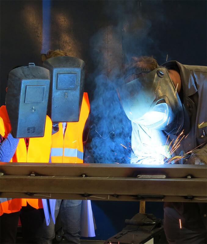 Students watching an instructor working on a project in a welding educational facility.