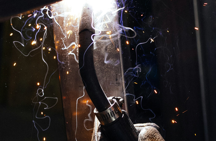 A welder's hand wearing a protective glove and welding on a project in a confined space.