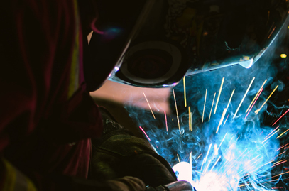 Welder working on a galvanized steel project while fumes and smoke emit into the surrounding area.
