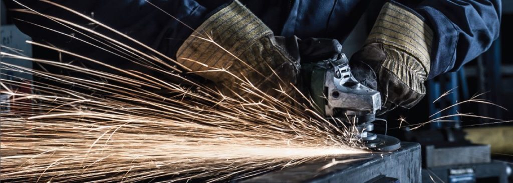 A burst of sparks being emitted during a grinding and deburring application. The gloved hands of a welder holding onto a grinder tool.